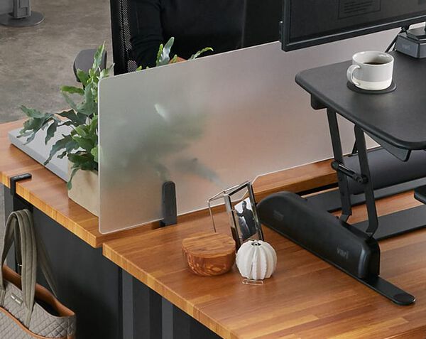 acrylic privacy panel attached to a table next to a varidesk converter