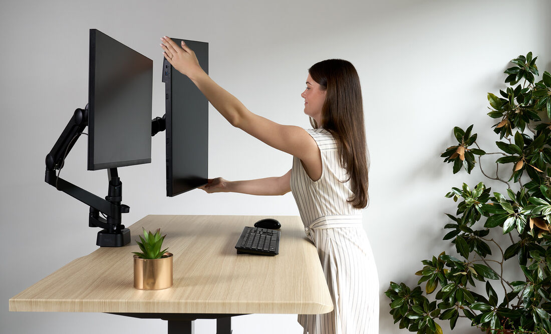 woman standing in front of an electric standing adjusting one of the two monitors that are installed on the dual monitor arm