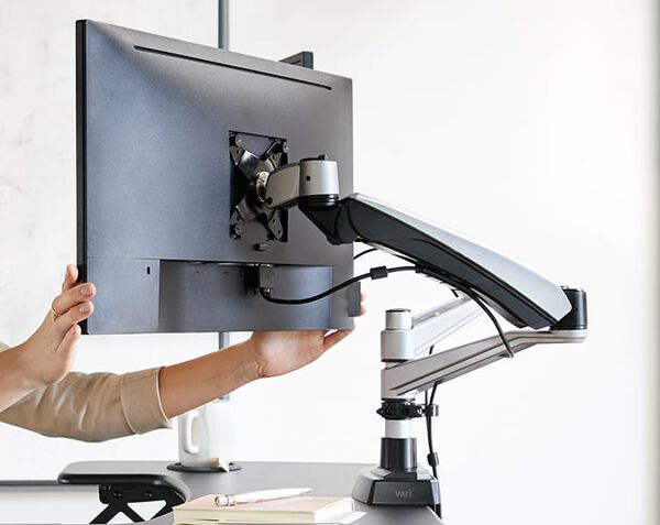Close up view of monitor arm attached to desk in office being adjusted