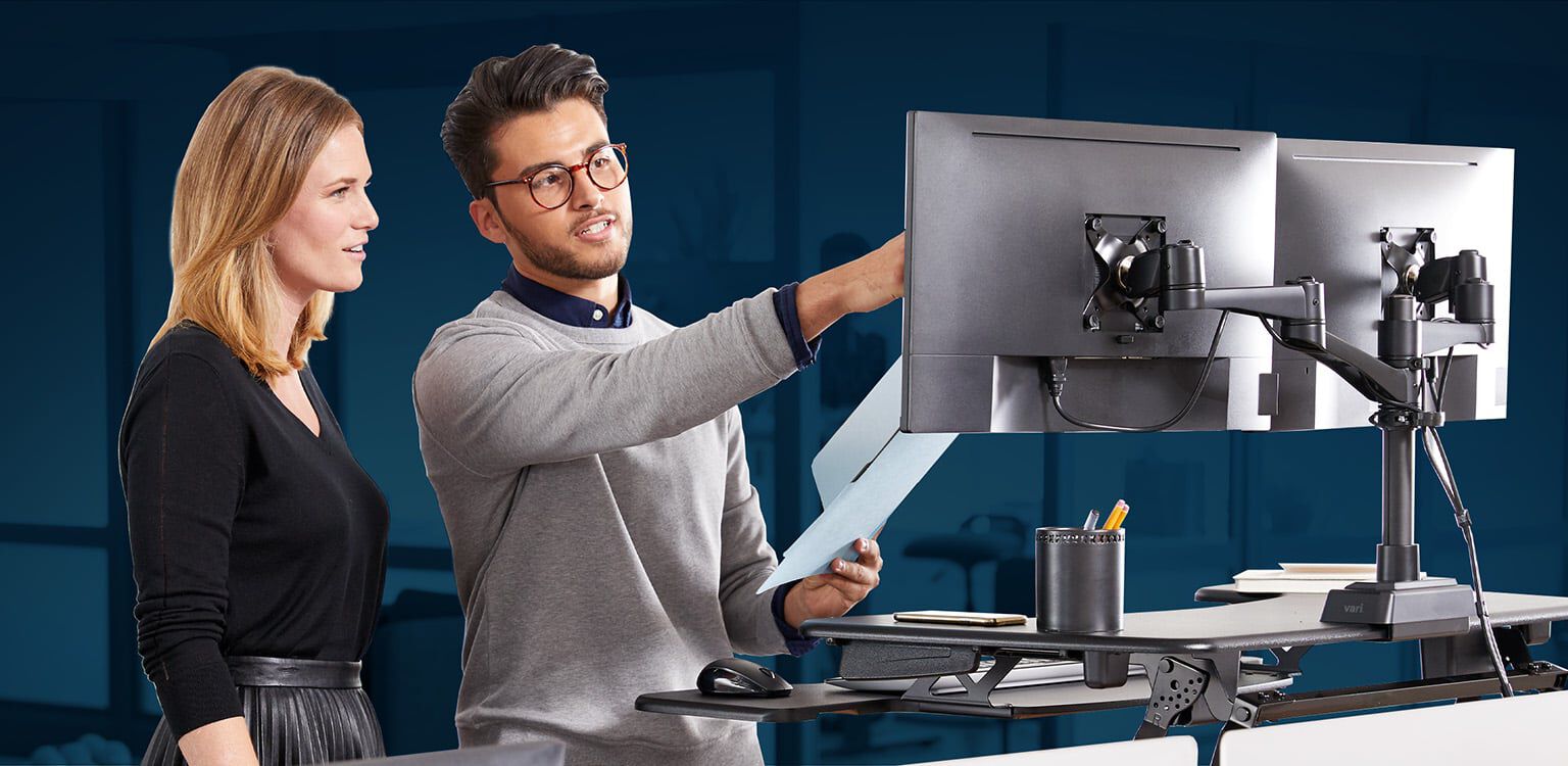 Professional at VariDesk Converter with two monitors raised in office