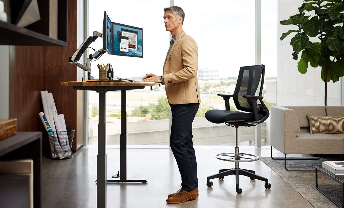 Individual standing at full electric desk working in an office setting overlooking cityscape