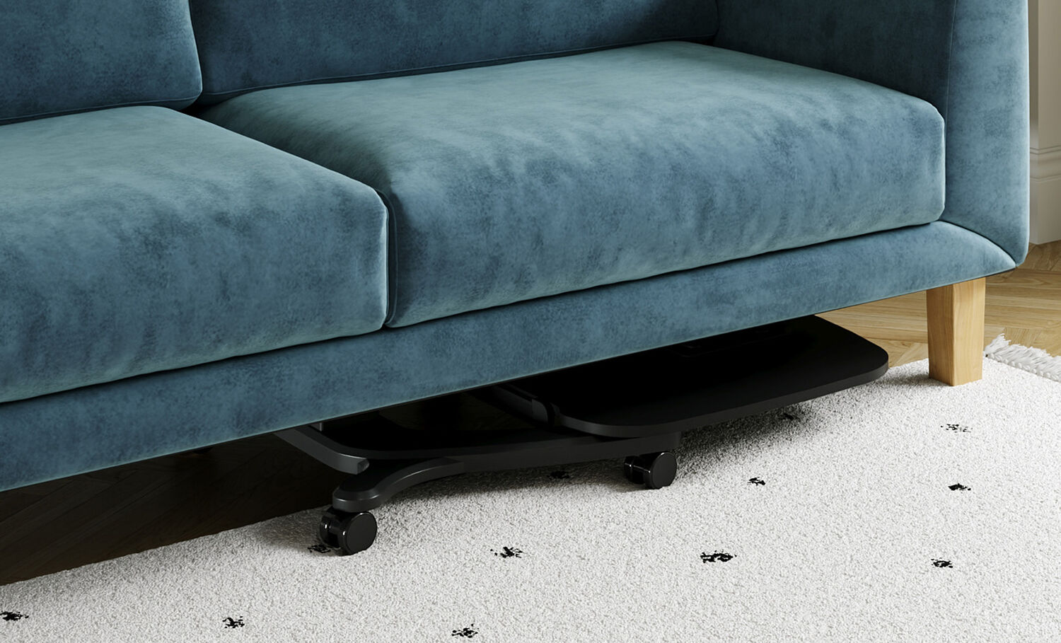Close-up of the mobile laptop desk's low-profile tabletop and caster wheels tucked beneath a teal velvet sofa, demonstrating its ability to slide under furniture for storage.