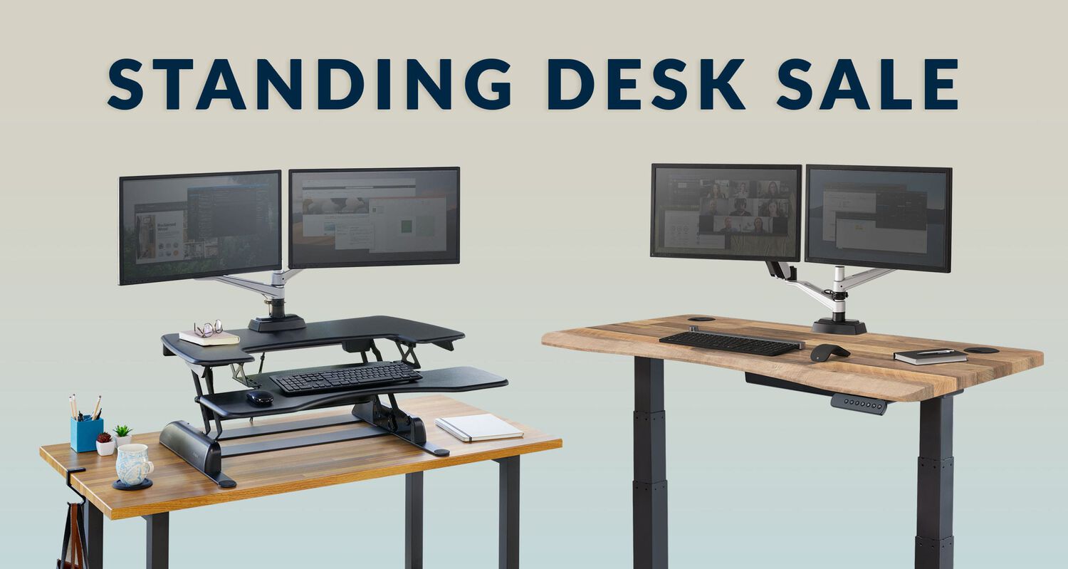 vari electric standing desk in reclaimed wood with dual monitor arms and varidesk converter in black on top of a reclaimed wood table