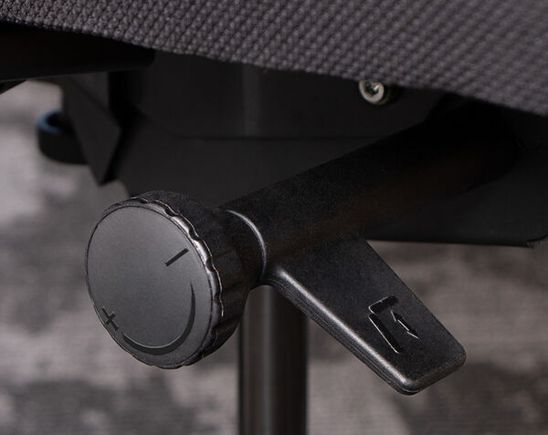 Close-up of Vari TempurPedic ergonomic office chair’s adjustment mechanism, showing a tension control knob with plus and minus symbols and a lever beneath the seat for reclining or tilt adjustment.