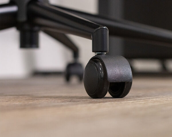 Close-up of the black caster wheel on the office chair's base, resting on a wood floor.
