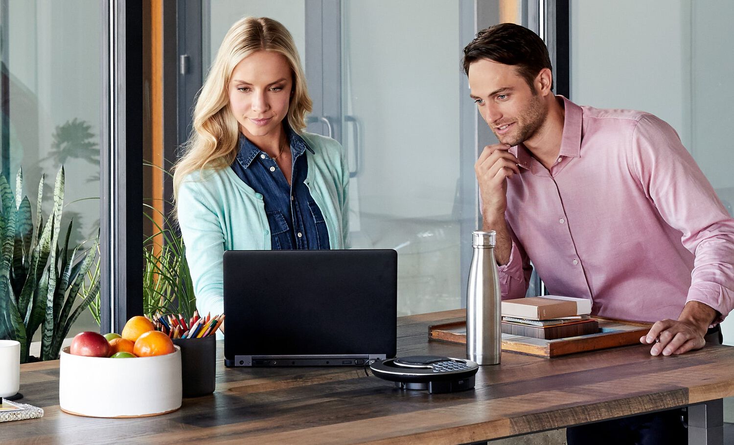 two professionals standing at conference table reviewing laptop screen
