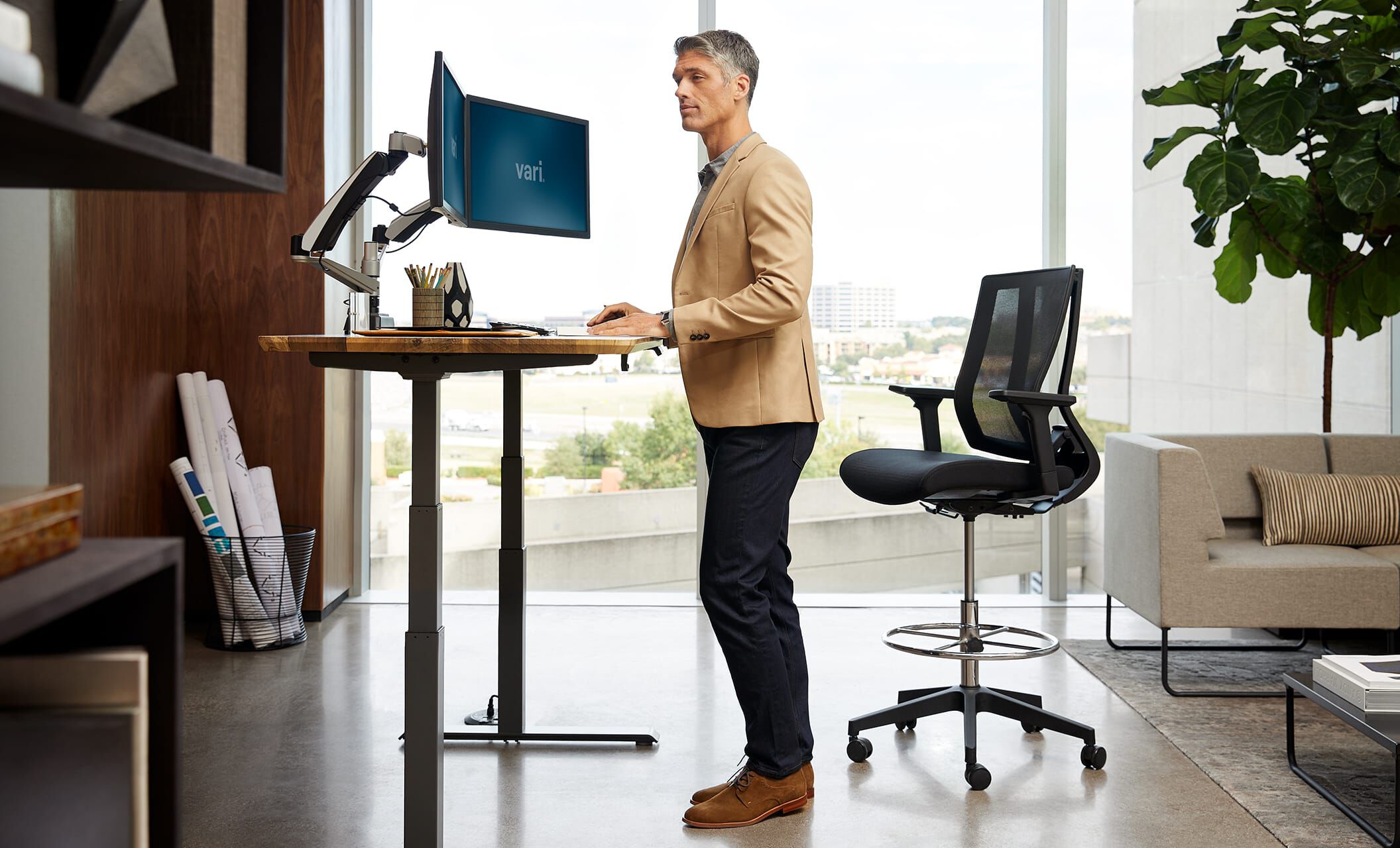 Individual standing at full electric desk working in an office setting overlooking cityscape
