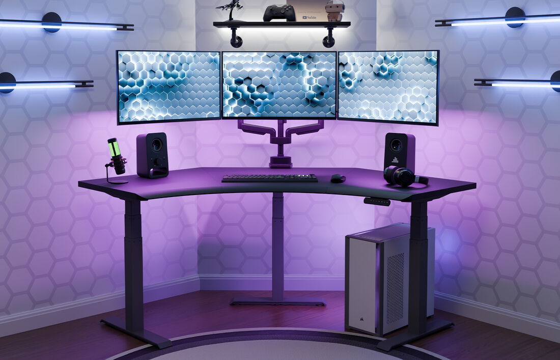 A sleek gaming setup featuring the Vari Command Center Electric Standing Desk with triple monitors displaying a hex pattern, purple LED lighting, a standing desk, microphone, speakers, headphones, and a white Corsair PC tower in a modern room.