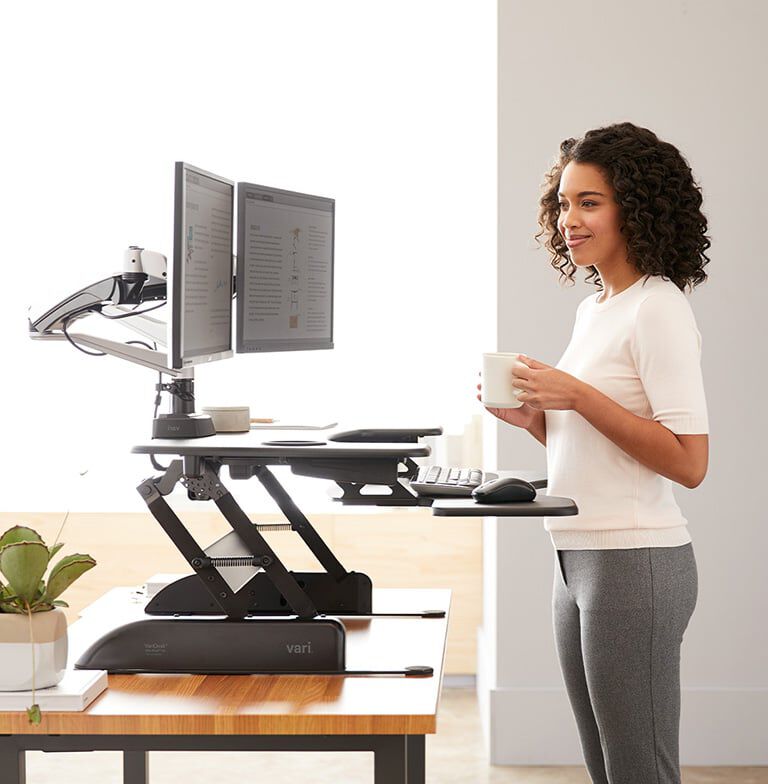 Professional standing at VariDesk Converter with two monitors in office