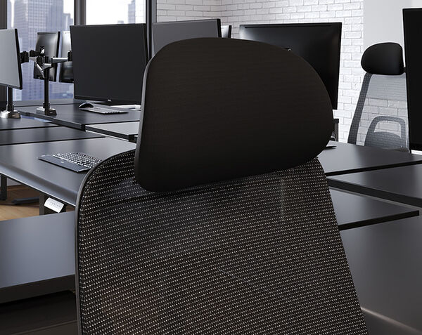 Rear view of a black fabric headrest mounted on a mesh office chair, in an open office with monitors, keyboards, and a whiteboard in the background.