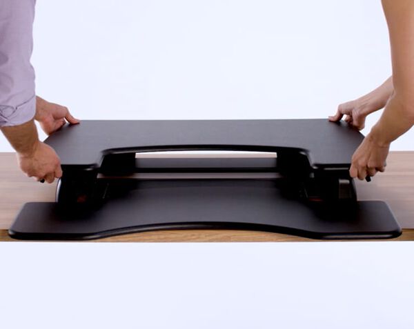 Two individuals lifting desk riser onto exsisting desk