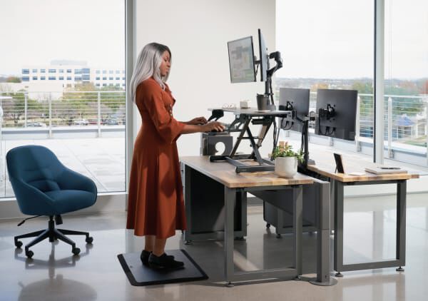 Individual standing at varidesk converter on top of existing desk in office