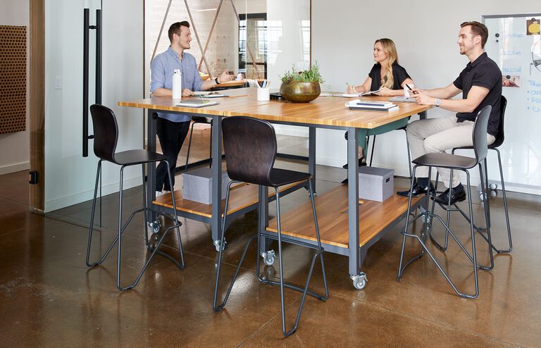 Three professionals in conference room, some are sitting in Wood Conference Chairs during meeting