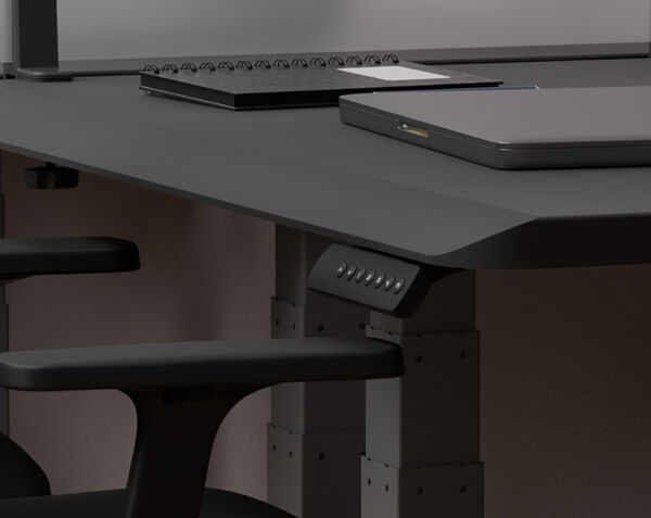 A compact home office setup featuring a black electric standing desk in a cozy alcove, with a modern computer monitor, a black stool, and decorative elements like framed art and a mirror.