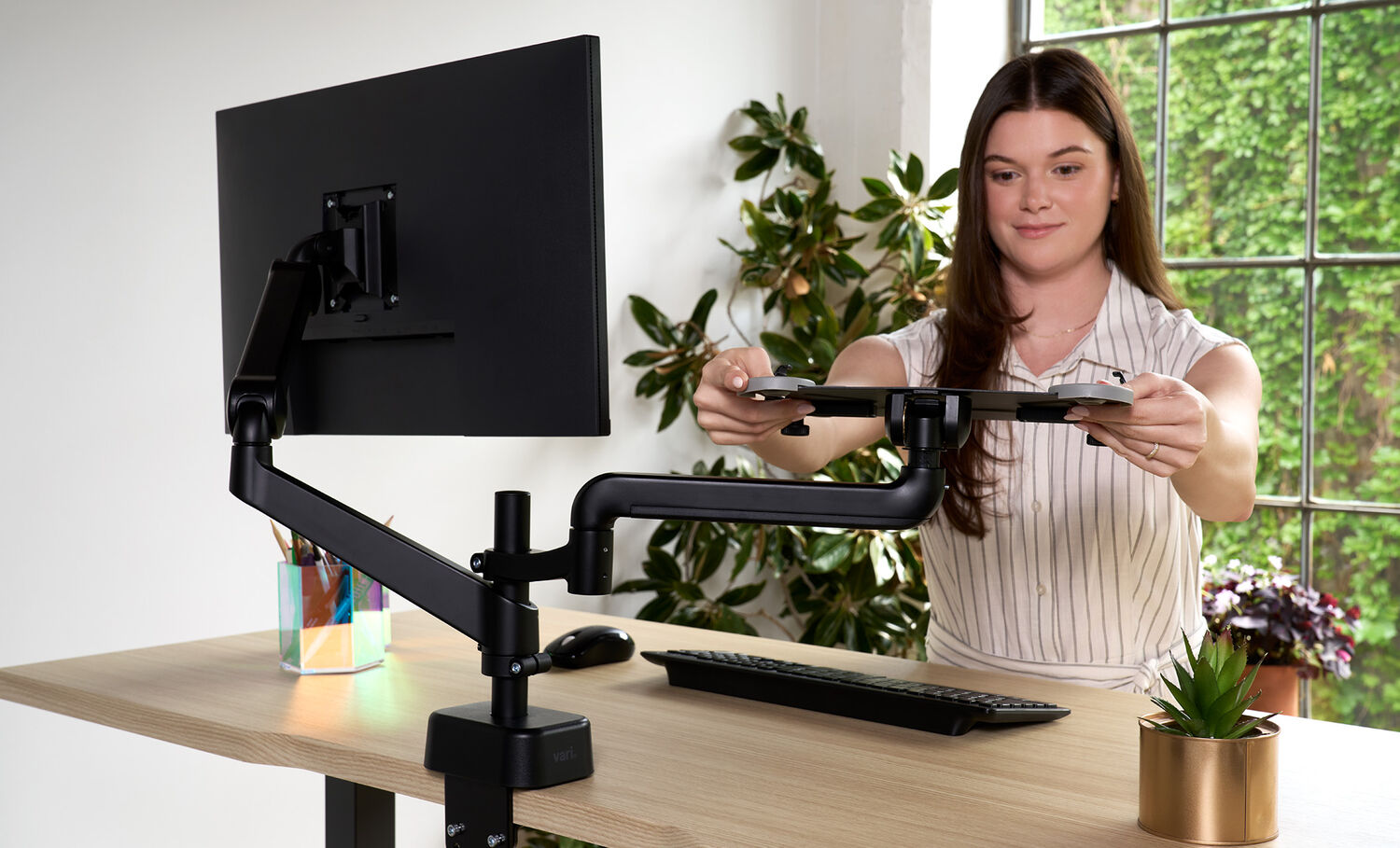 woman attaching the laptop holder to a single monitor arm with the post installed on a desk in a home environment 