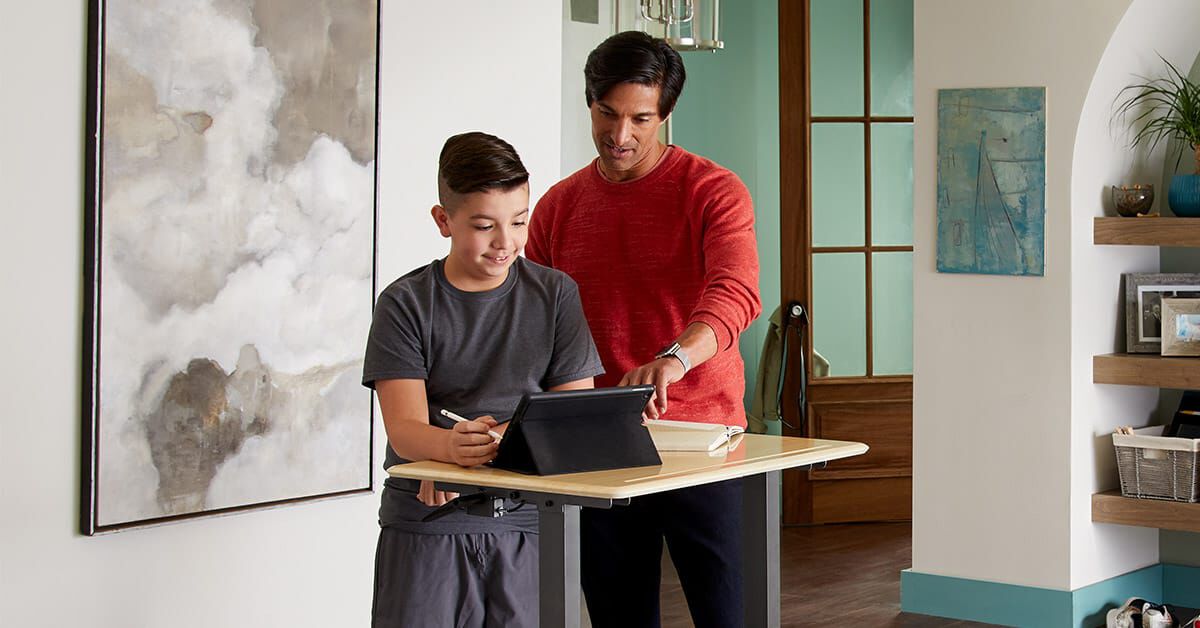 parent helping high school student working at vari classroom desk in home setting