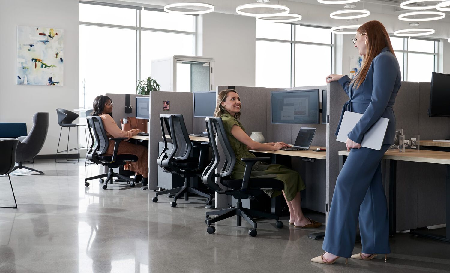 two women talking while at a workspace in an office setting