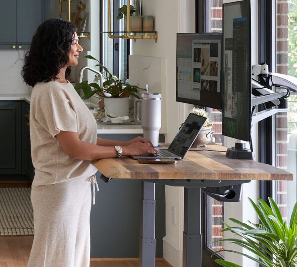 individual standing at an electric standing desk in a home office setting working