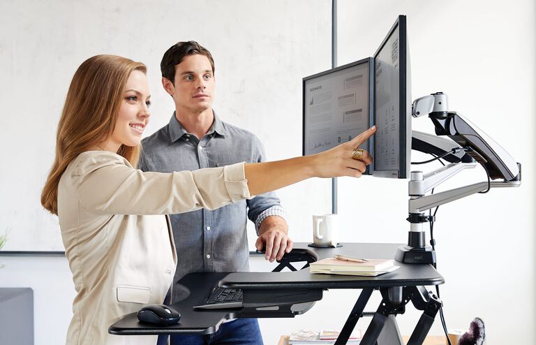 Two people looking at computer monitors on monitor arms attached to VariDesk Converter in an office