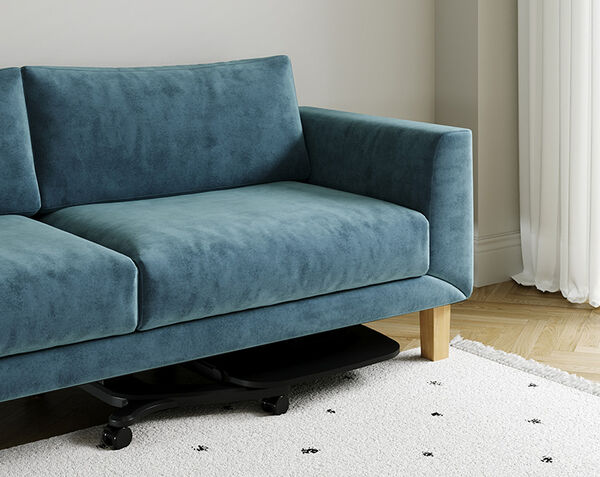 Close-up of the mobile laptop desk's black tabletop and caster wheels tucked beneath a teal velvet sofa on a white shag rug.