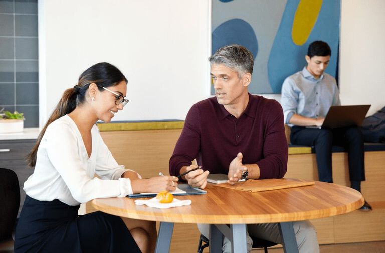 Two professionals working side by side with another individual working alone in a lounge office setting.
