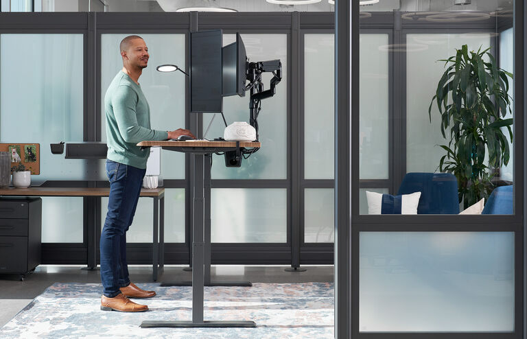 workspace setup with triple monitor arms on an electric standing desk with the user standing and looking across the span of the screens