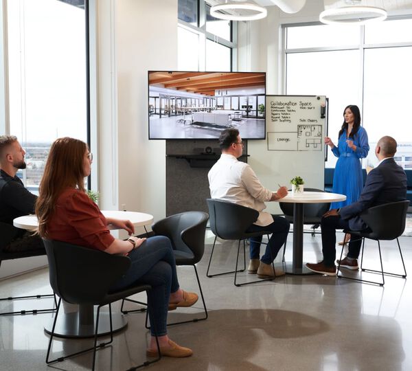 group of individuals sitting at tables looking up at one person presenting at a white board