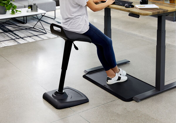 professional perched on active seat at electric standing desk