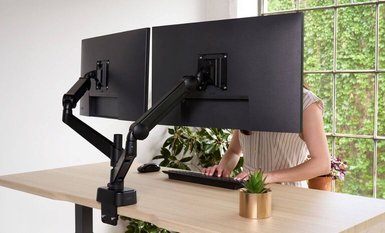 Two people looking at computer monitors on monitor arms attached to VariDesk Converter in an office