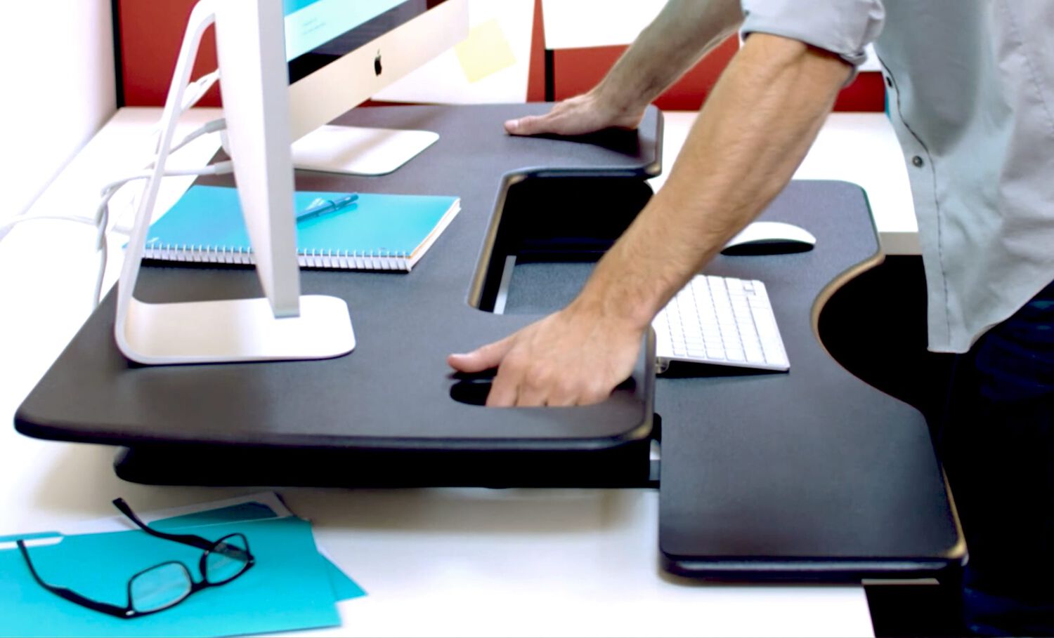 Individual using hands to raise desktop converter from lowered position to raised position with two monitors on the top of the desktop converter