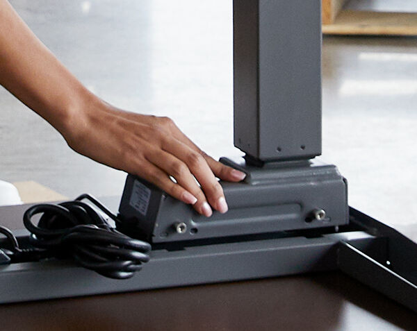 Individual is assembling the Electric Standing Desk 60x30 by locking the legs of the desk into place with one hand