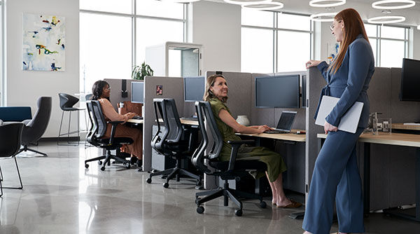 two women talking while standing and sitting in an office cubicle