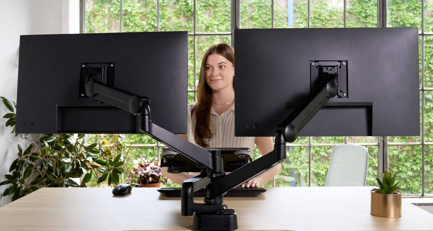 person using a standing desk and dual monitor arms
