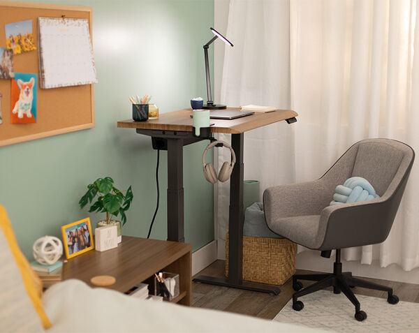 A row of three black electric standing desks with frosted privacy screens, each set up with a laptop, arranged in a modern office with large windows showing a cityscape.