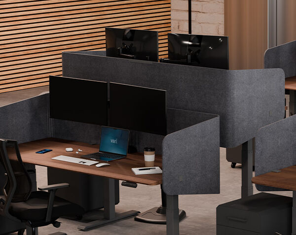 The felt privacy desk surround 72 is setup on an electric standing desk in a lowered position in front of another electric standing desk in raised position
