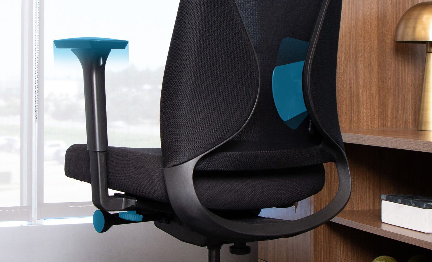 Close-up of the backside of the Vari TempurPedic Chair in black ergonomic office chair highlighting adjustable features, including armrests, lumbar support, and seat controls, set beside a wooden bookshelf and a window with a bright outdoor view.
