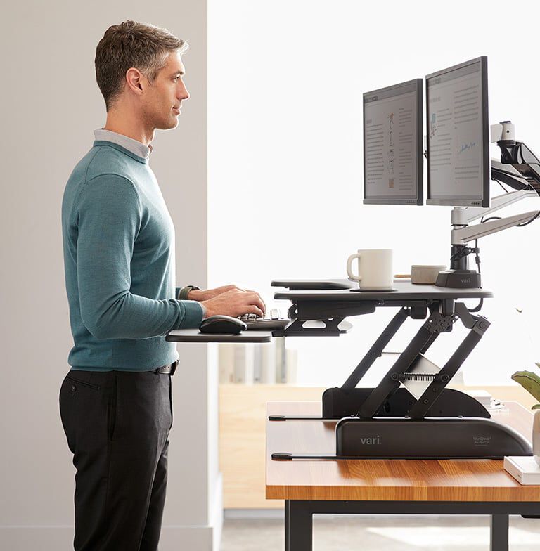 Professional standing at VariDesk Converter raised in office with two monitors