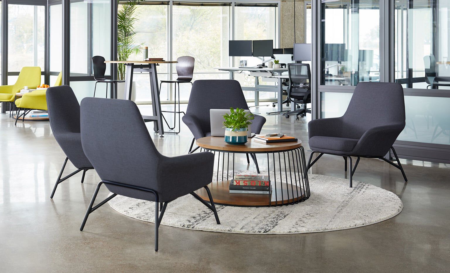 in an open offic, there's a casual meeting space with four chairs facing eachother for easy meetings. The chairs have mid-height backs and low arms with upholstery on all surfaces.
