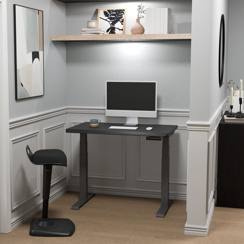 Black electric standing desk lowered in a stylish home office nook with a monitor, keyboard, and ergonomic stool. image number null