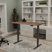 Electric Standing Desk 60x30 with tech track in walnut with slate legs in lowered position at home