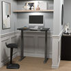 Black electric standing desk raised in a stylish home office nook with a monitor, keyboard, and ergonomic stool.