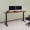 Electric standing desk 72x30 in walnut finish with black legs raised in office