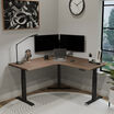 walnut finish l shape electric standing desk in a lowered position in the corner of a workspace