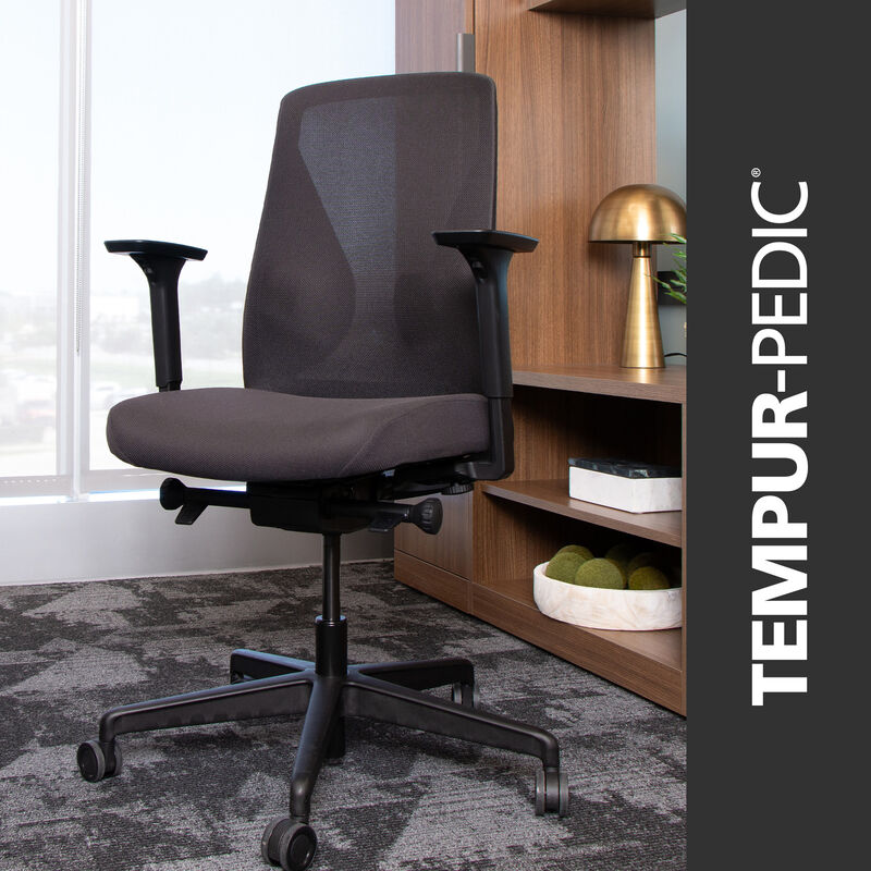 Dark Gray ergonomic Tempur-Pedic office chair from Vari with mesh back and adjustable armrests, shown in a modern office setting with wood shelving and decorative accents image number null