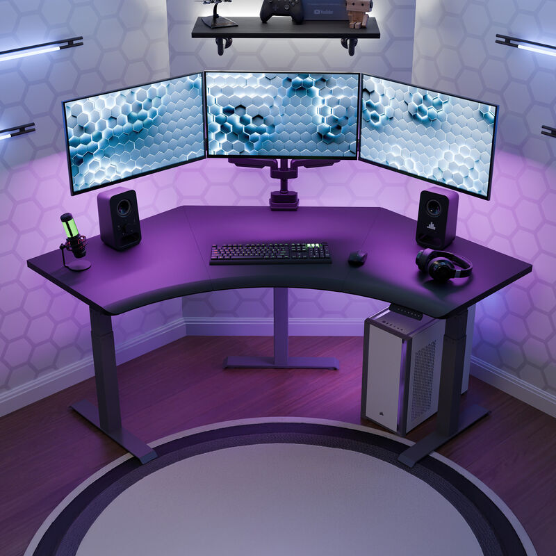 A gaming and streaming setup with a overhead view of a black finish command center electric standing desk, triple monitors, RGB lighting, and a sleek PC tower, all set against a hex-patterned wall with ambient LED strips. image number null