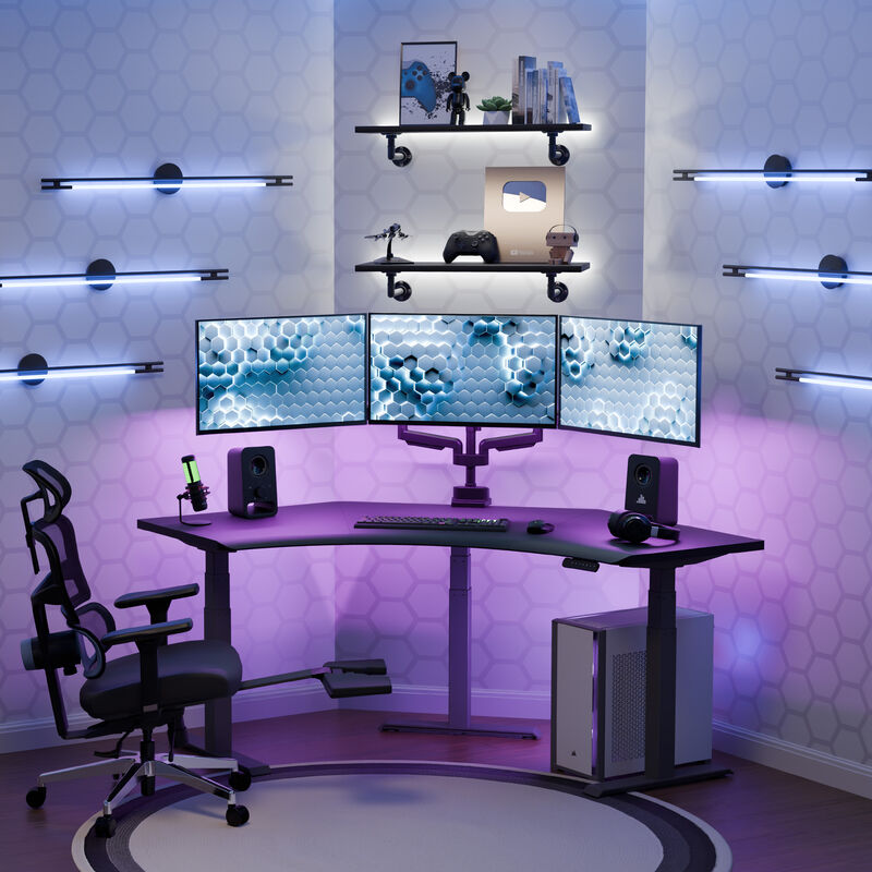 A gaming and streaming setup with a lowered position black finish command center electric standing desk, triple monitors, RGB lighting, and a sleek PC tower, all set against a hex-patterned wall with ambient LED strips. image number null
