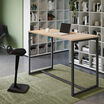 standing work table in light wood finish setup in an open workspace environment with an active seat and laptop in use on top of the table