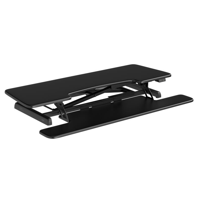 Angled product shot of a black electric standing desk converter partially raised, showing the work surface, keyboard tray, X-frame lift mechanism, and up and down height buttons, on a white background. image number null