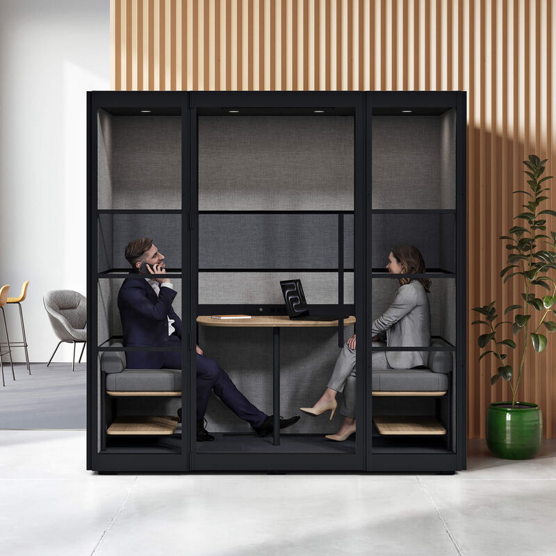 two person privacy booth in the black finish against a wall in an office with two individuals sitting and working inside image number null