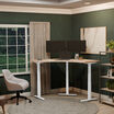 command center electric standing desk with a light wood desktop and white legs in a raised position 